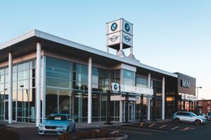 Luxurious car dealership showcasing BMW and MINI cars with a modern glass exterior at dusk.